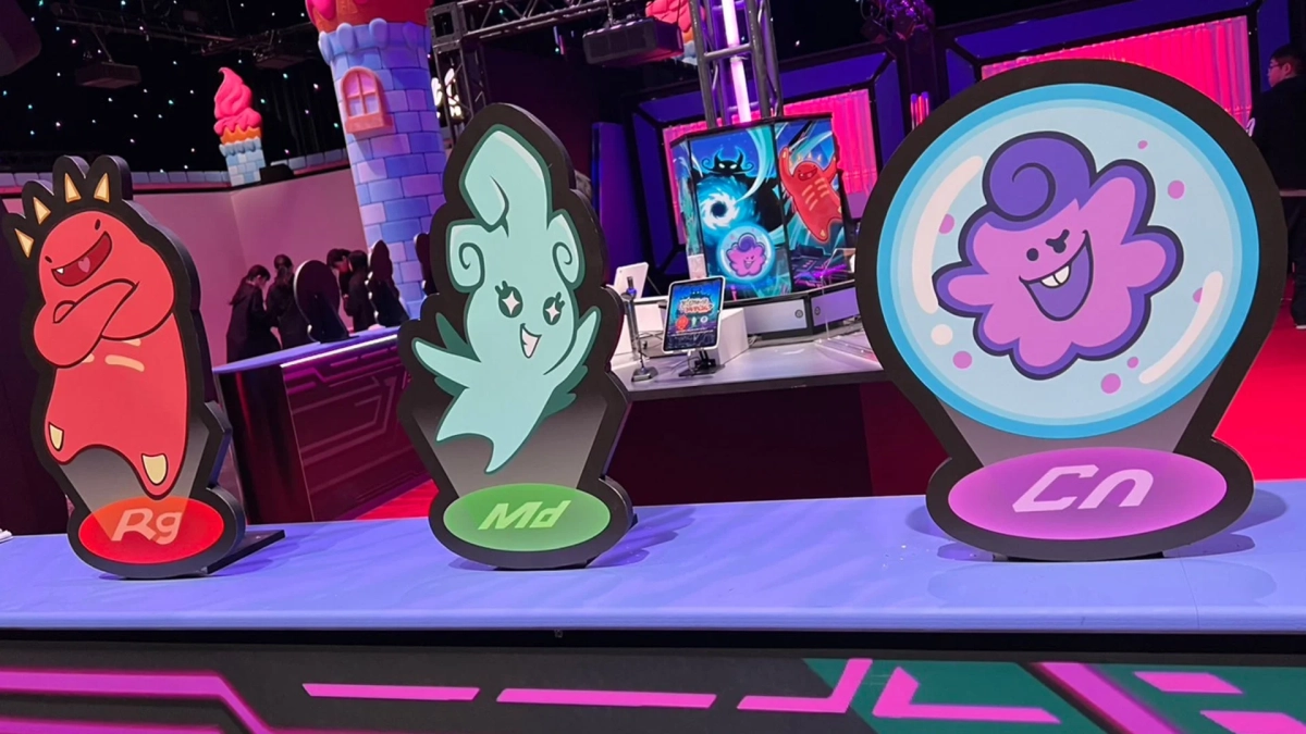 ゲームイベント会場のような場所で、3体のカラフルなモンスターキャラクターの等身大パネルが展示されています