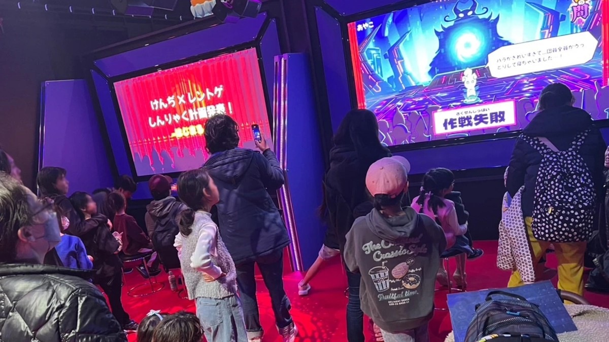 多くの人々、特に子供連れの家族が、鮮やかなデジタルスクリーンに映し出されたコンテンツを熱心に見ているイベント会場の様子