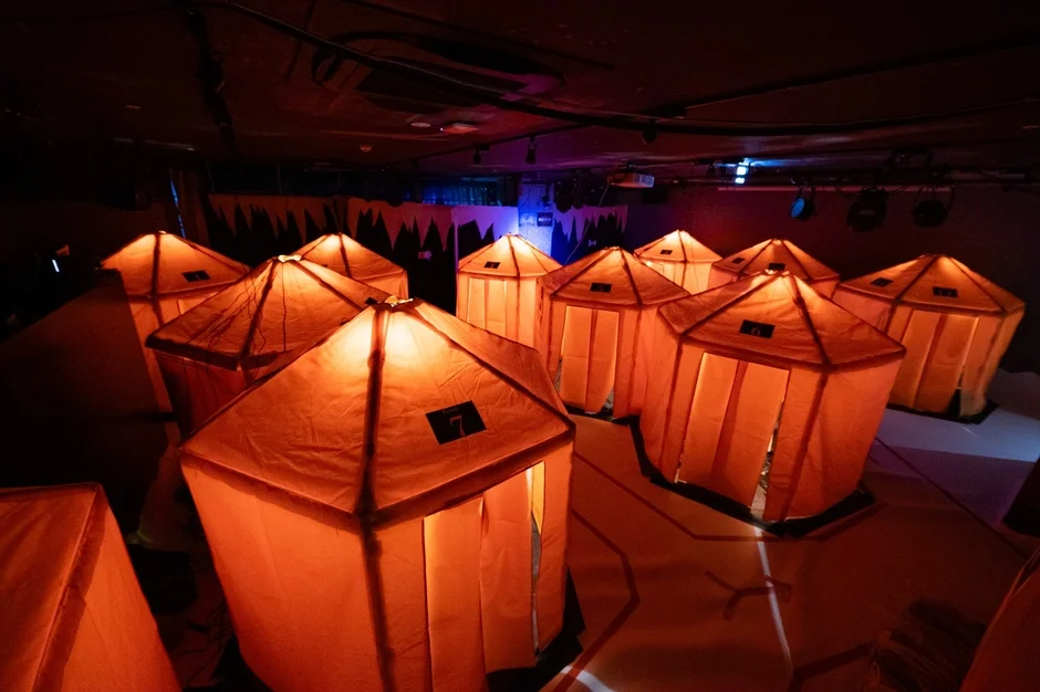 暗い屋内に複数のオレンジ色のテントのような構造物が並び、内部から暖かく光を放っています。