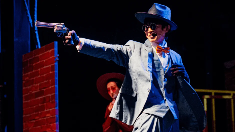 青いスーツの男性が拳銃を構える