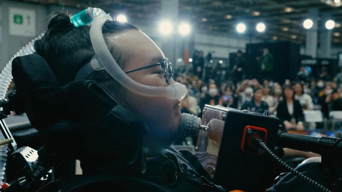 呼吸器と支援技術を装着した人物がイベントで集中している様子