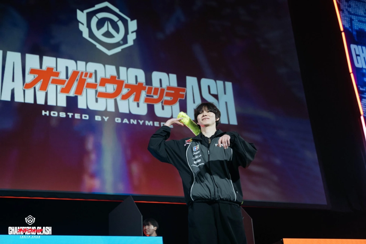 オーバーウォッチのeスポーツイベント「チャンピオンズクラッシュ」のステージ上で、笑顔の男性がパフォーマンスをしている様子です。