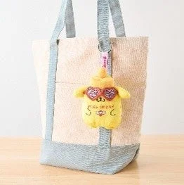 トートバッグに、ハート型のサングラスをかけたポムポムプリンのぬいぐるみキーホルダーがぶら下がっている様子
