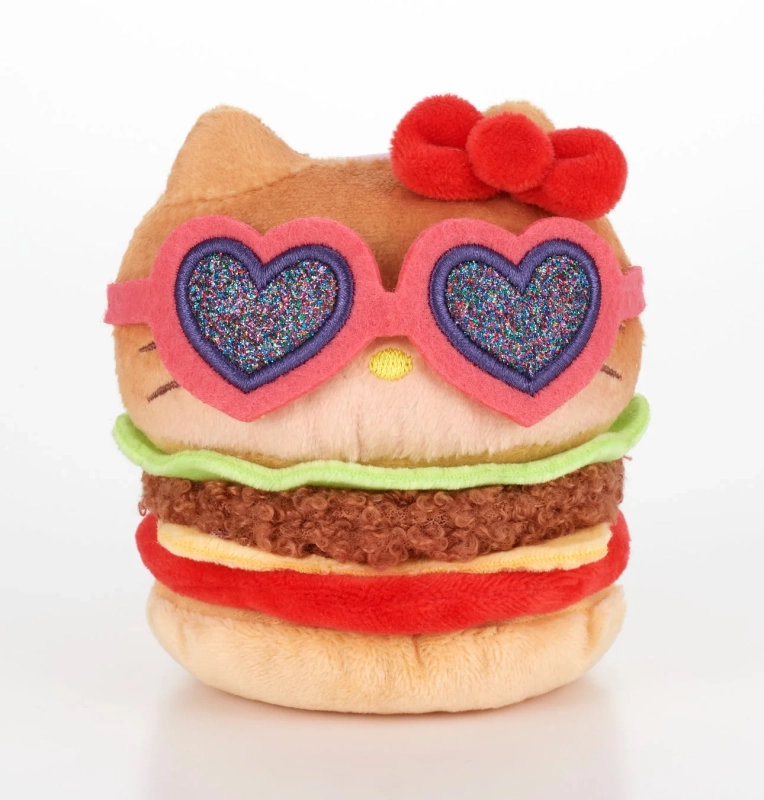 ハローキティがハンバーガーの形をしたぬいぐるみで、ハート型のグリッターサングラスと赤いリボンを身につけている