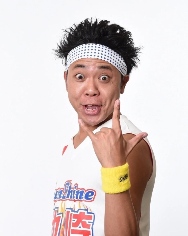 白いヘッドバンドと黄色いリストバンドを身につけた男性が、驚いたような表情でカメラを見つめ、片手でロックサインのポーズをとっています。シャツには「Sunshine」の文字が見えます。