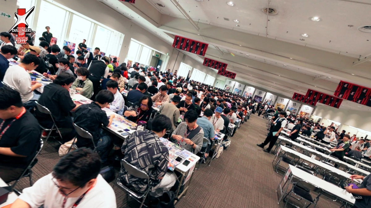 大勢の参加者がテーブルでカードゲームを楽しんでいるイベント会場の様子