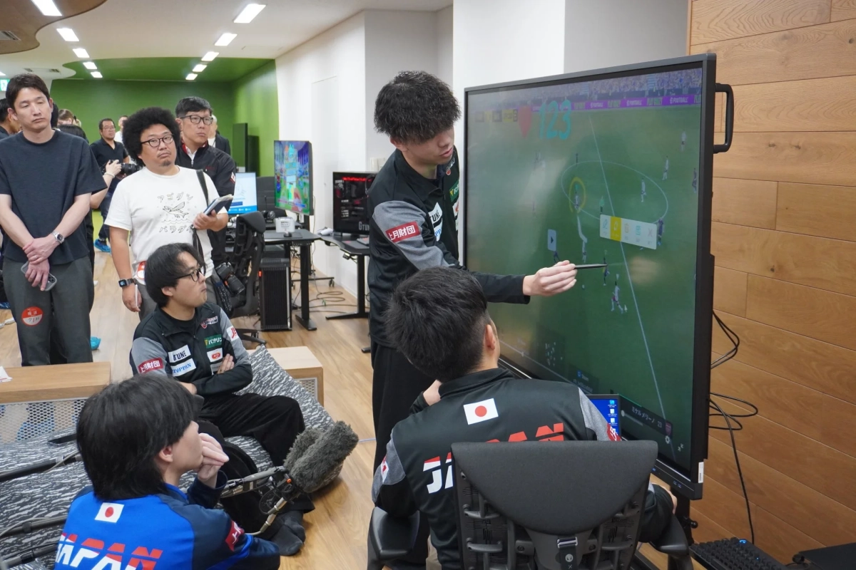 eスポーツのサッカーゲームをプレイする選手たちが大画面モニターを見ながら戦略を話し合っている様子