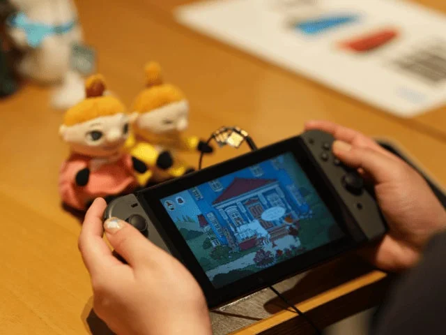 Nintendo Switchを操作する人物とムーミンぬいぐるみ