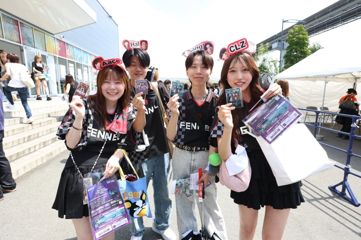 FENNELのシャツを着た4人の若者が、屋外のeスポーツイベントで笑顔でポーズをとっています