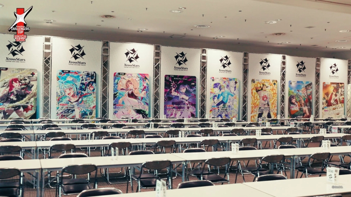 XrossStars CHALLENGERS CUPのイベント会場の様子。壁面にはトレーディングカードゲーム「XrossStars」の大型カードが展示され、会場には多数のテーブルと椅子が並べられている