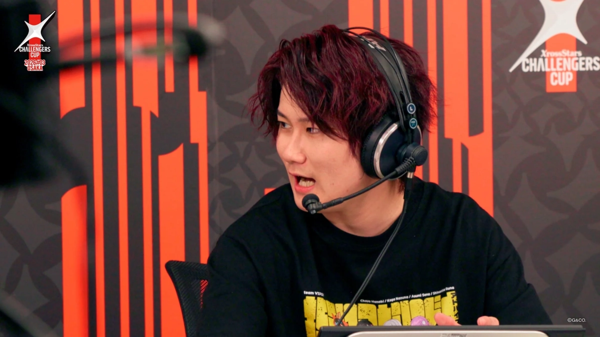 ゲーミングヘッドセットを装着した赤髪の男性が、XrossStars CHALLENGERS CUPのロゴがある背景の前で話している様子