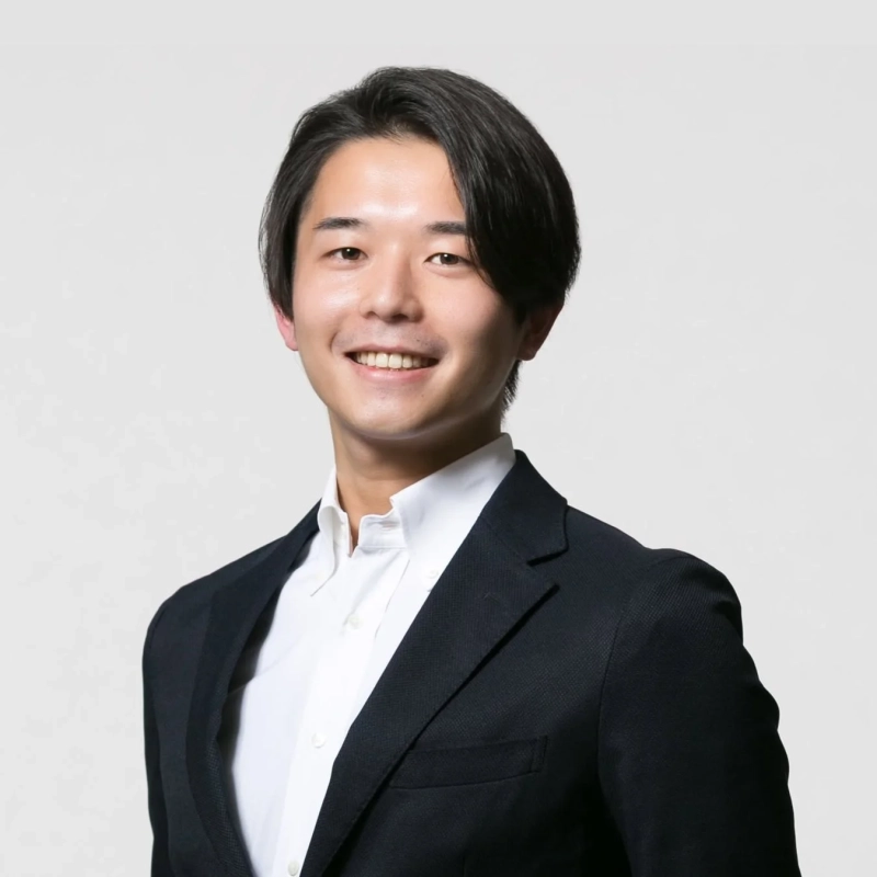 黒いスーツと白いシャツを着用し、笑顔でカメラを見つめる若いアジア人男性